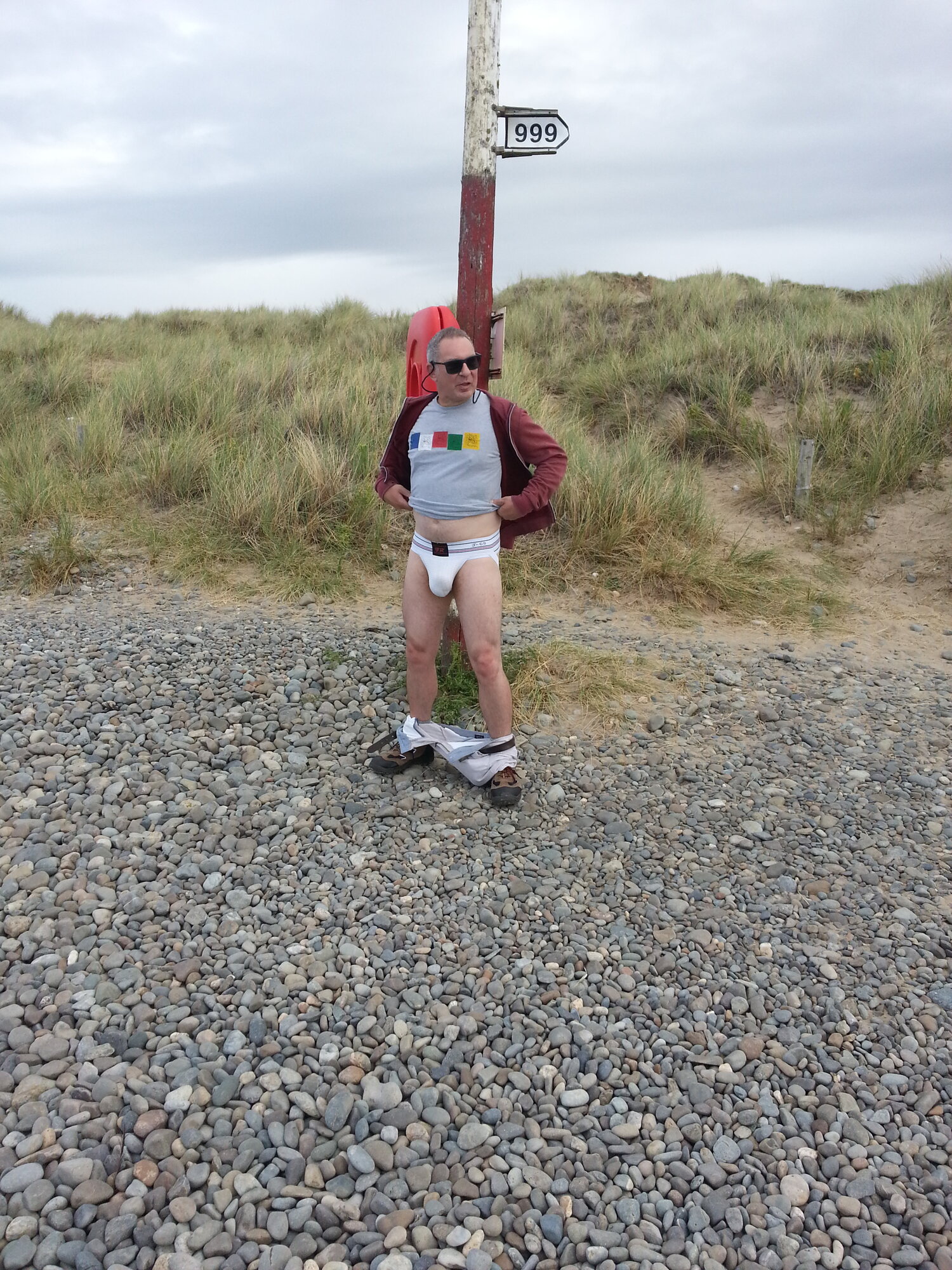 Standing against the emergency 999 signpost wearing white F&R #2 jockstrap